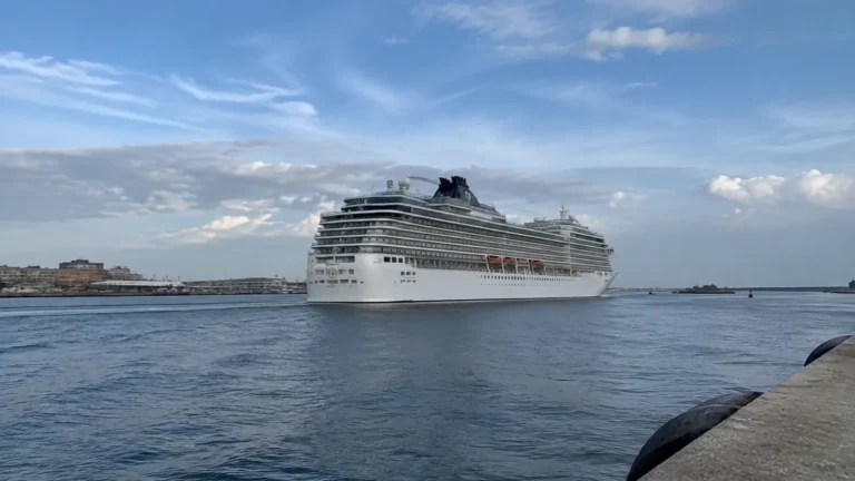 Large white cruise ship passing through calm harbor water.
