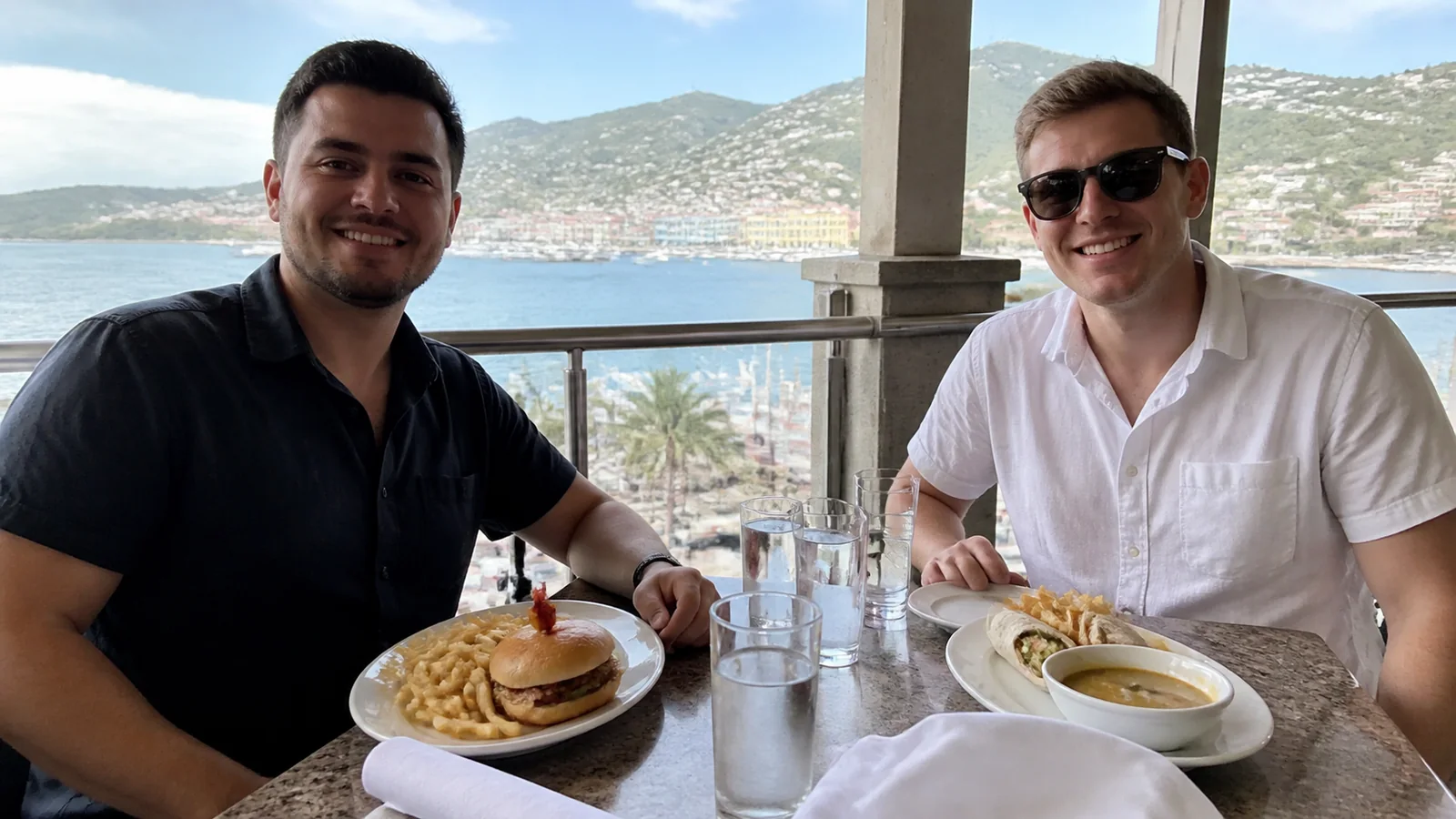 Two men dining together at a waterfront restaurant table.