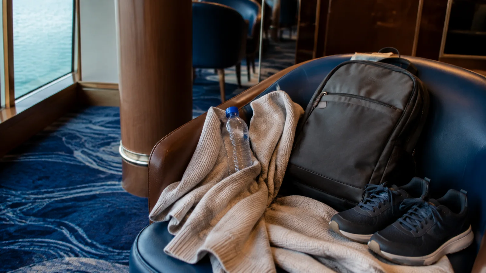 Backpack, water bottle, cardigan, and walking shoes arranged on a lounge chair.