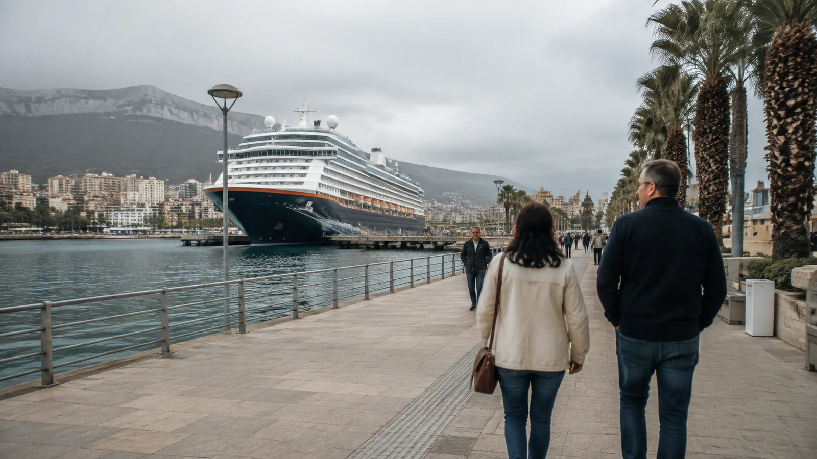 Couple walking along a waterfront promenade toward a docked cruise ship.
