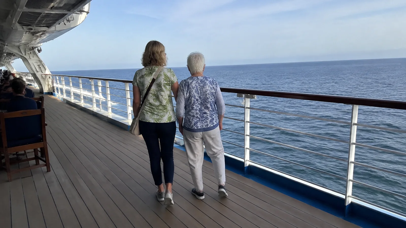 Two older women walking together along an outside ship deck.