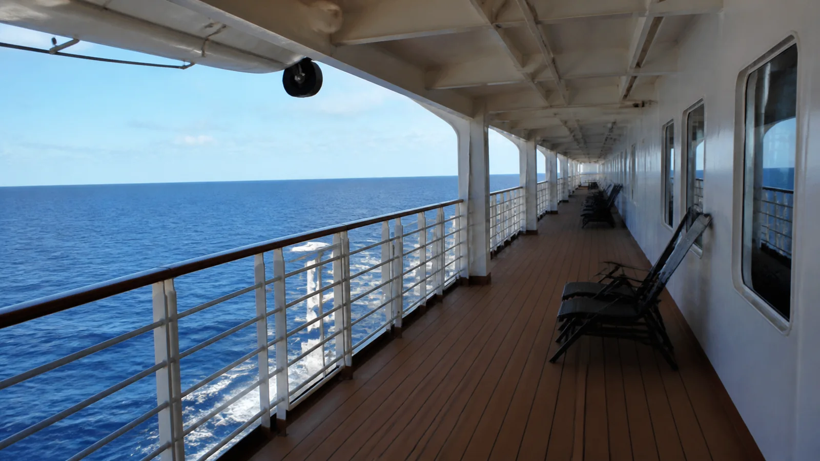 Quiet covered ship promenade with empty chairs overlooking the sea.