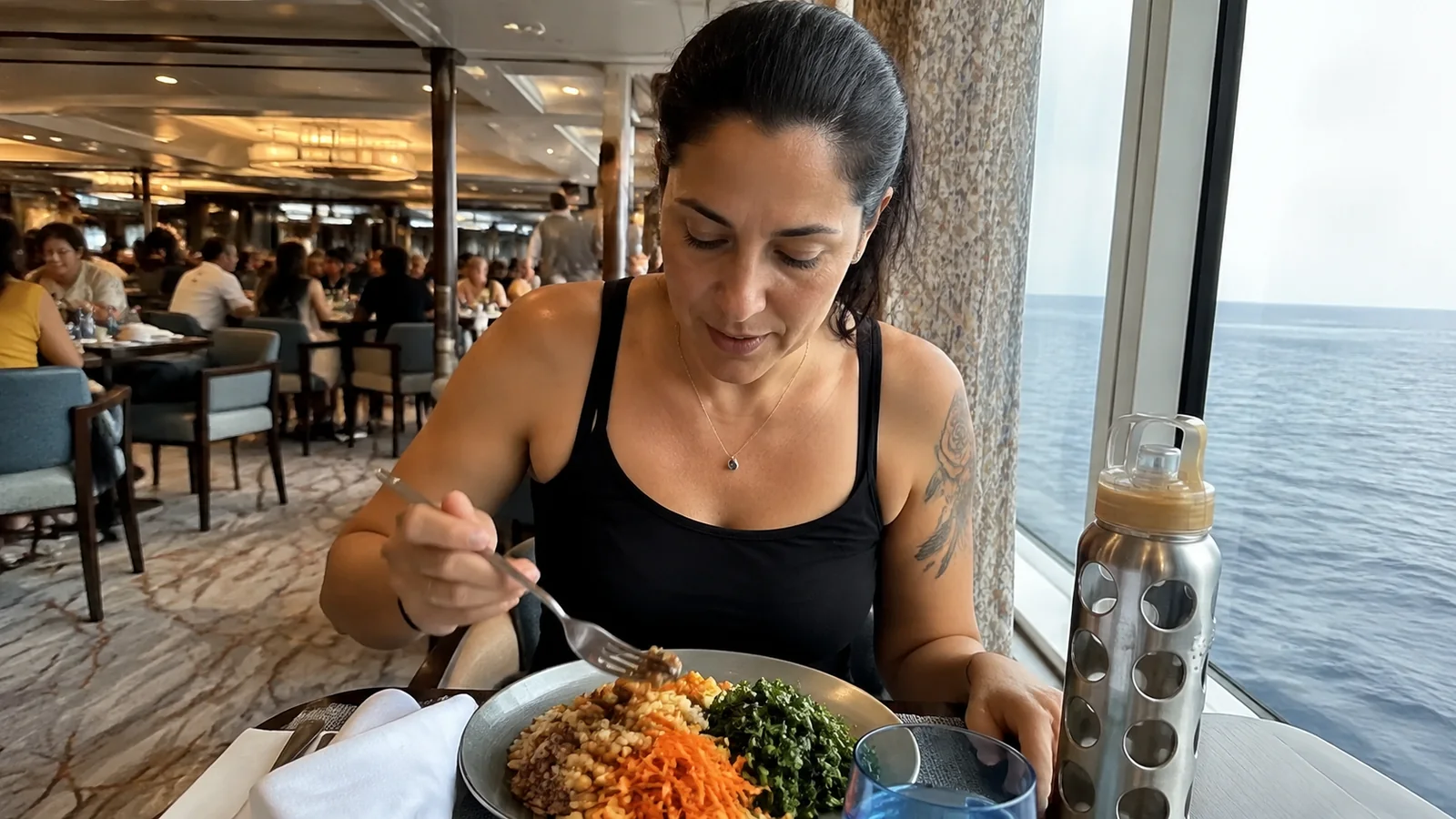 Woman eating a plated meal in a busy ship restaurant.