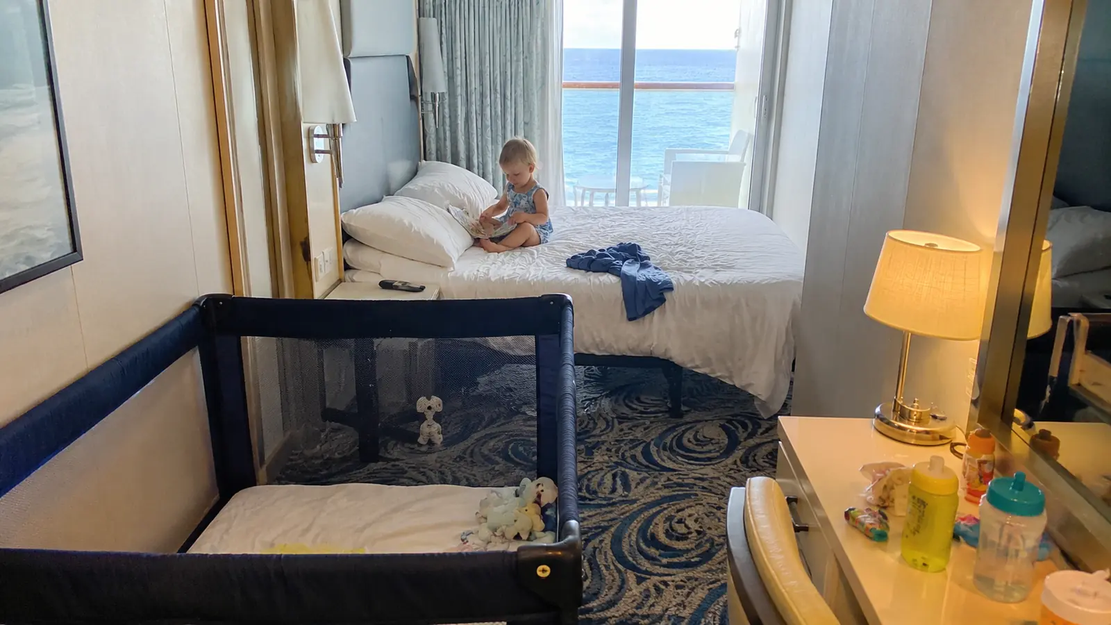 Cruise cabin with a portable crib and a toddler sitting on the bed