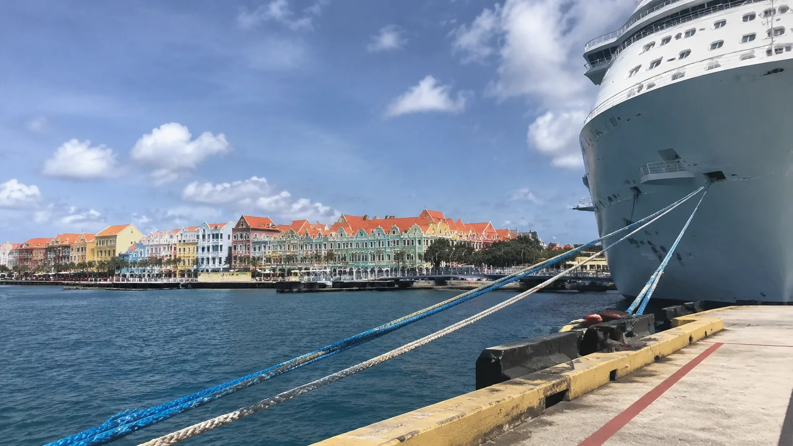 Cruise ship bow and mooring ropes with colorful waterfront buildings across the harbor