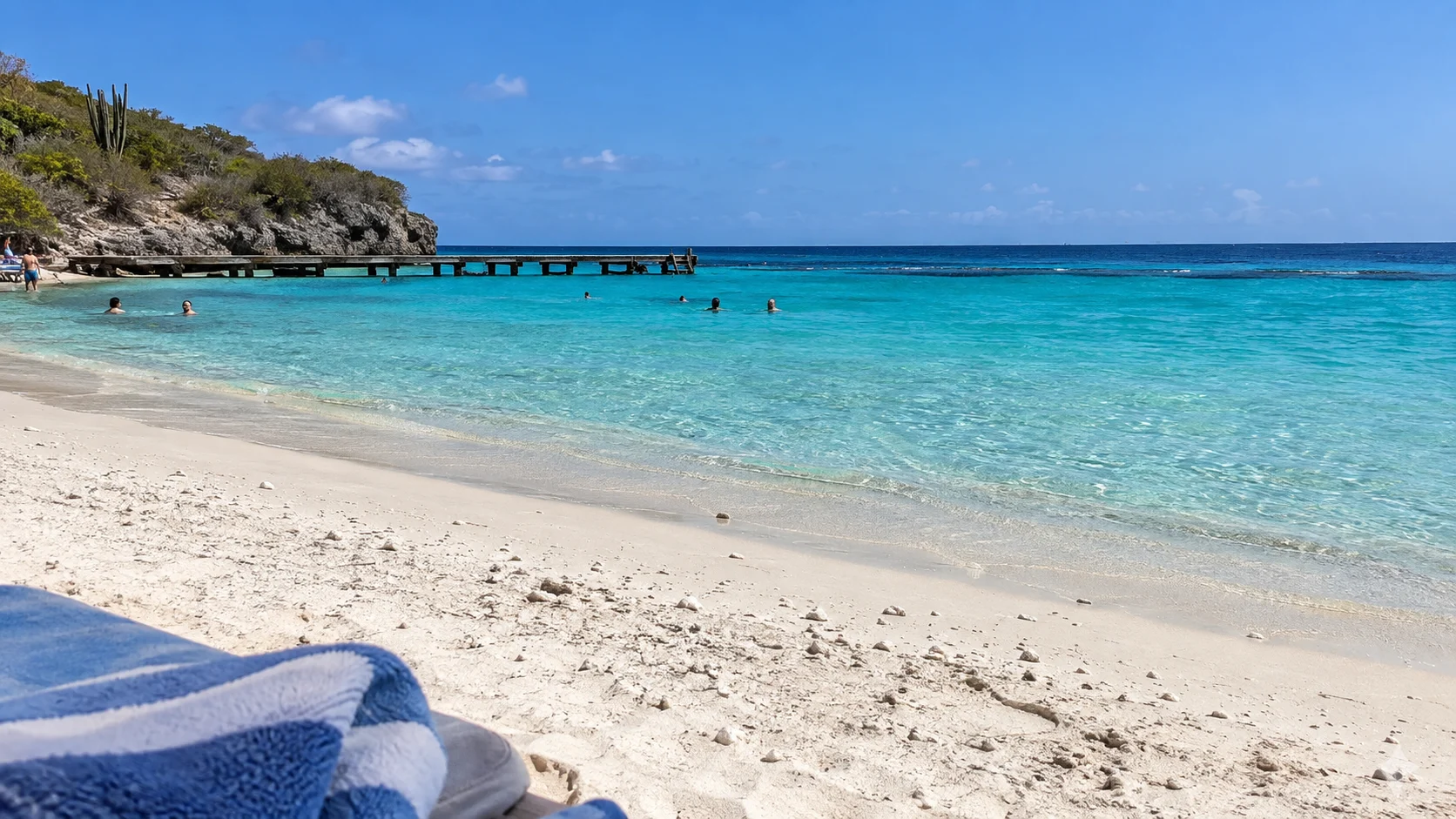 White coral sand, clear snorkeling water, and a wooden pier at Playa Porto Mari in Curaçao