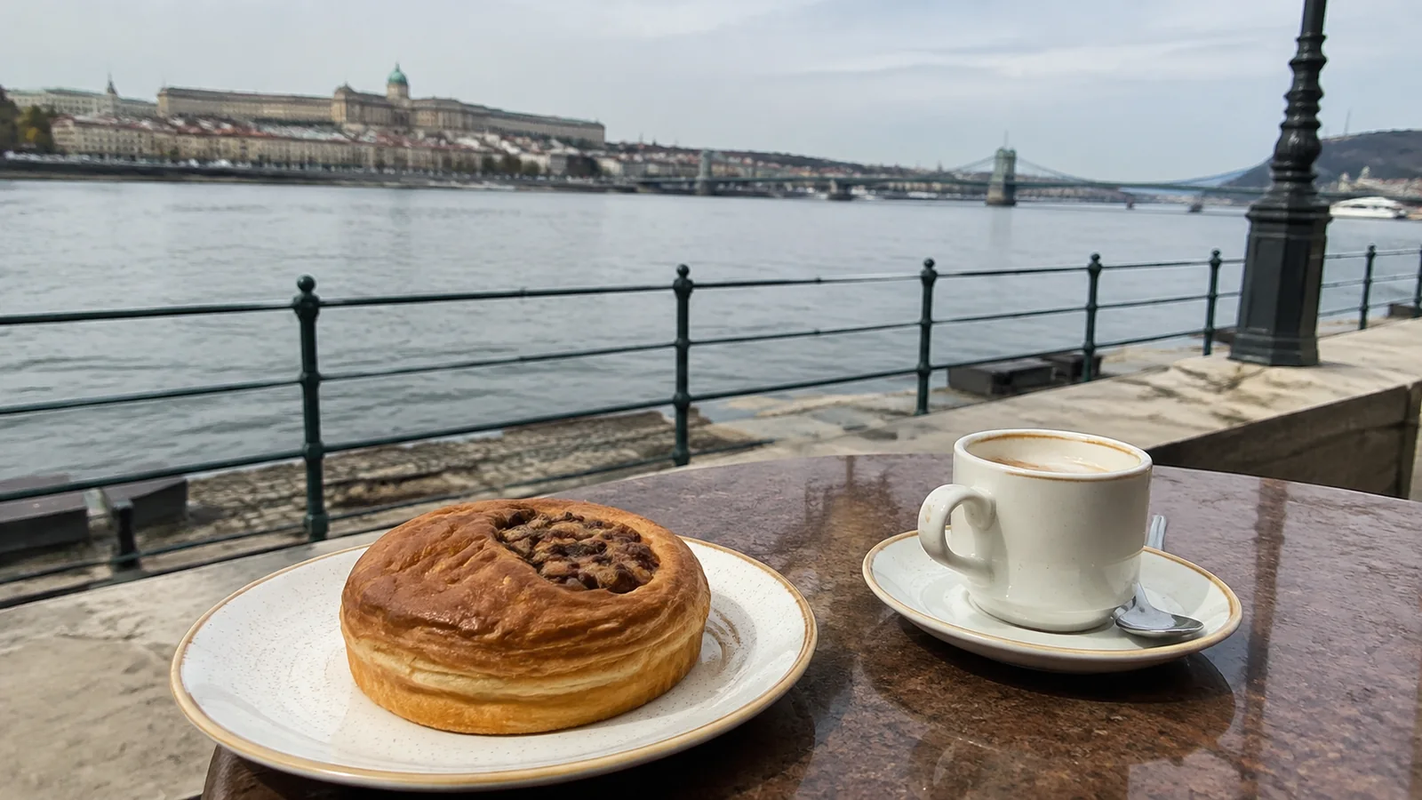 Pastry and coffee on an outdoor table beside a river railing.