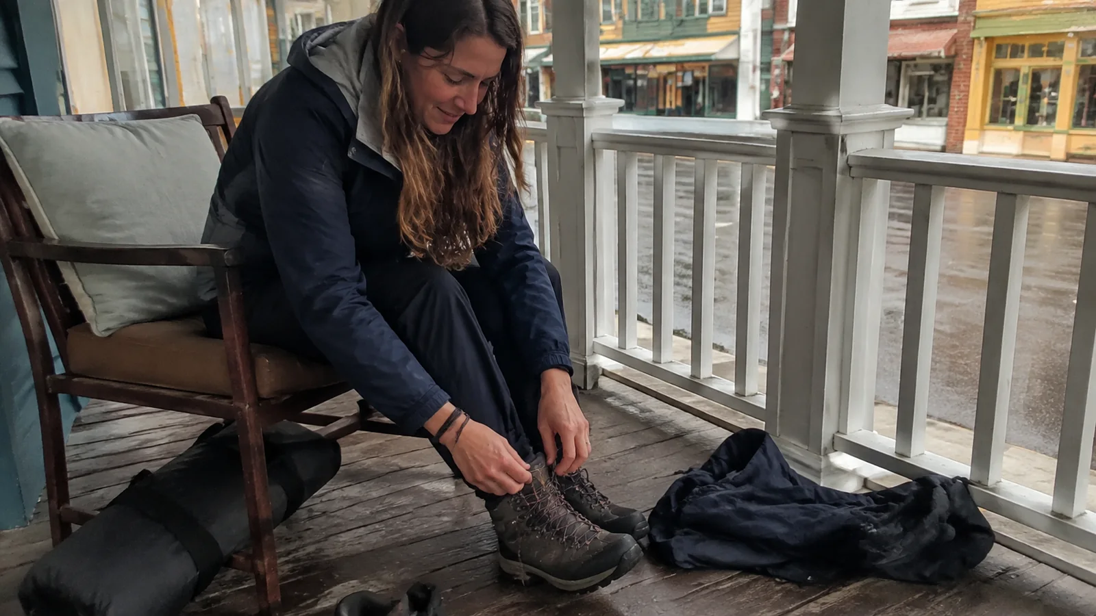 Woman ties her hiking boots while seated on a porch.