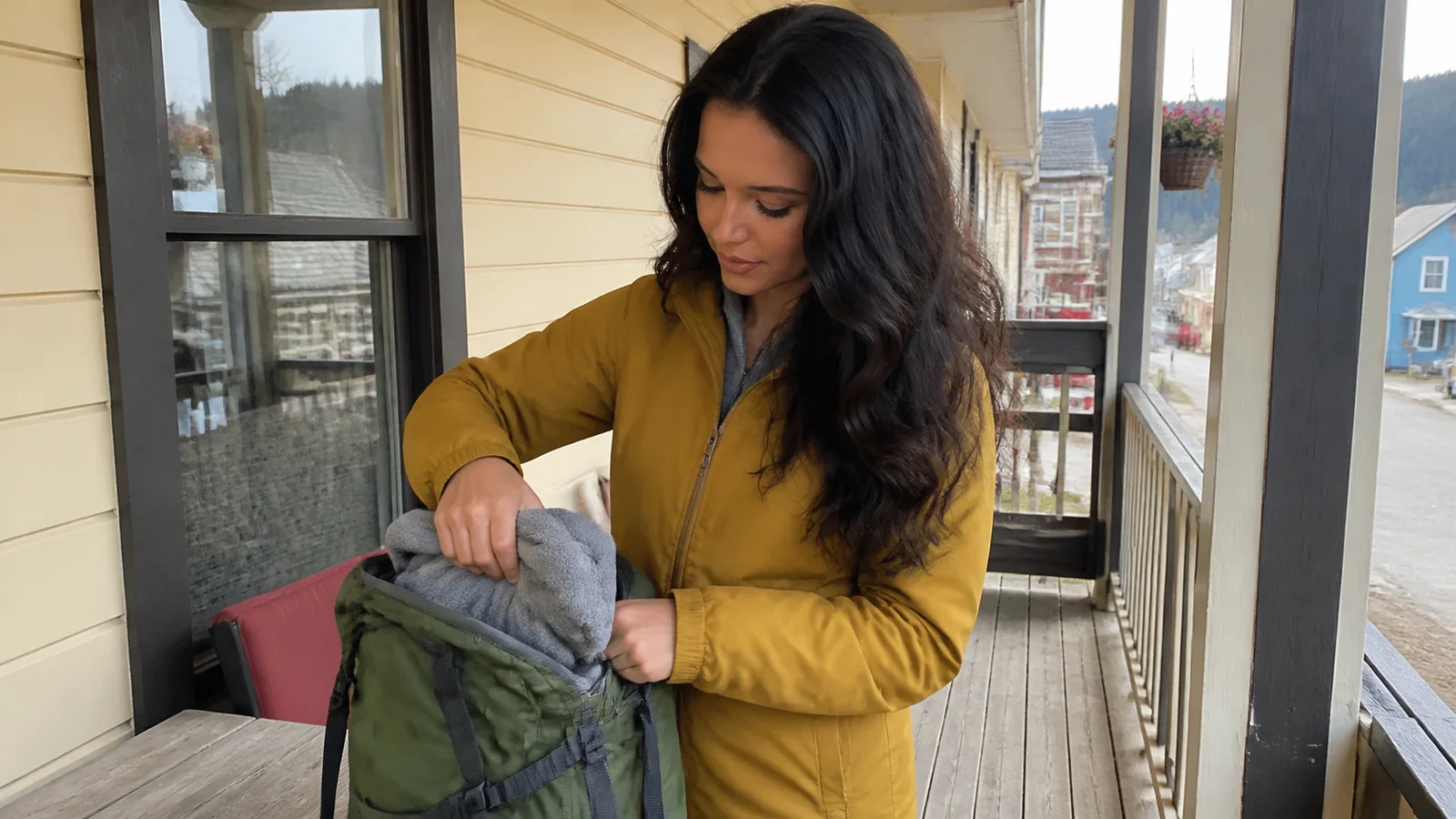 Woman packs a jacket into a backpack on a wooden porch.