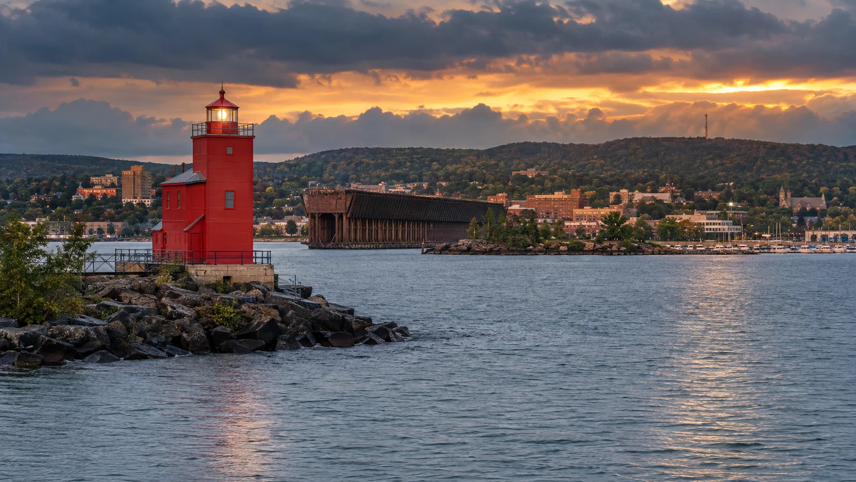 Red Marquette Harbor Lighthouse and historic ore dock beneath a dramatic sunset