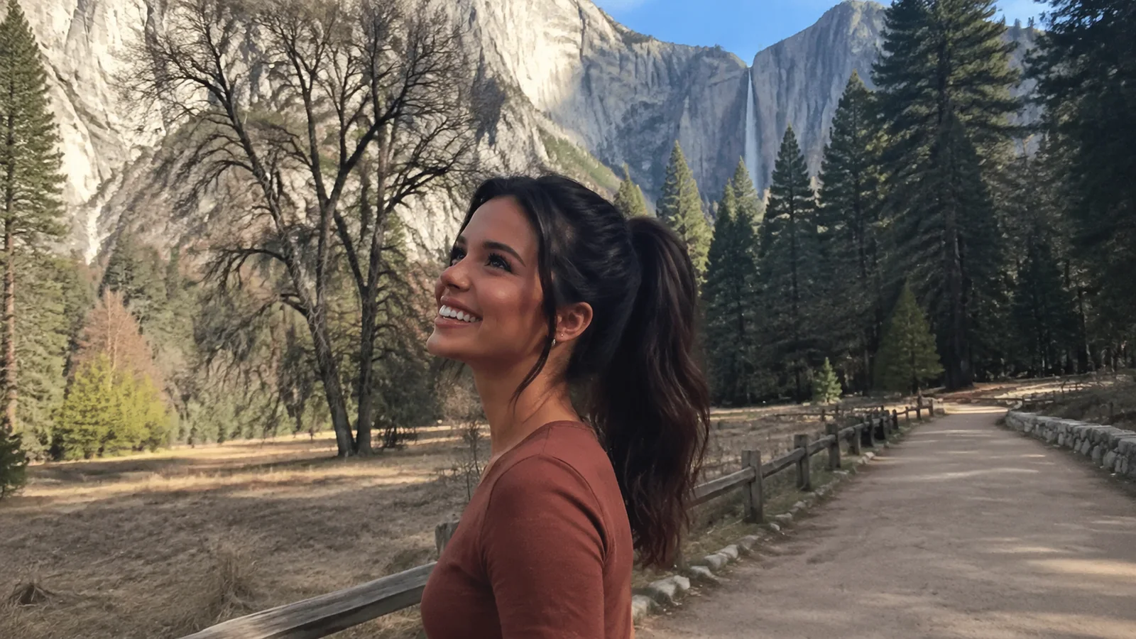 Woman walks beside a meadow beneath tall granite cliffs.