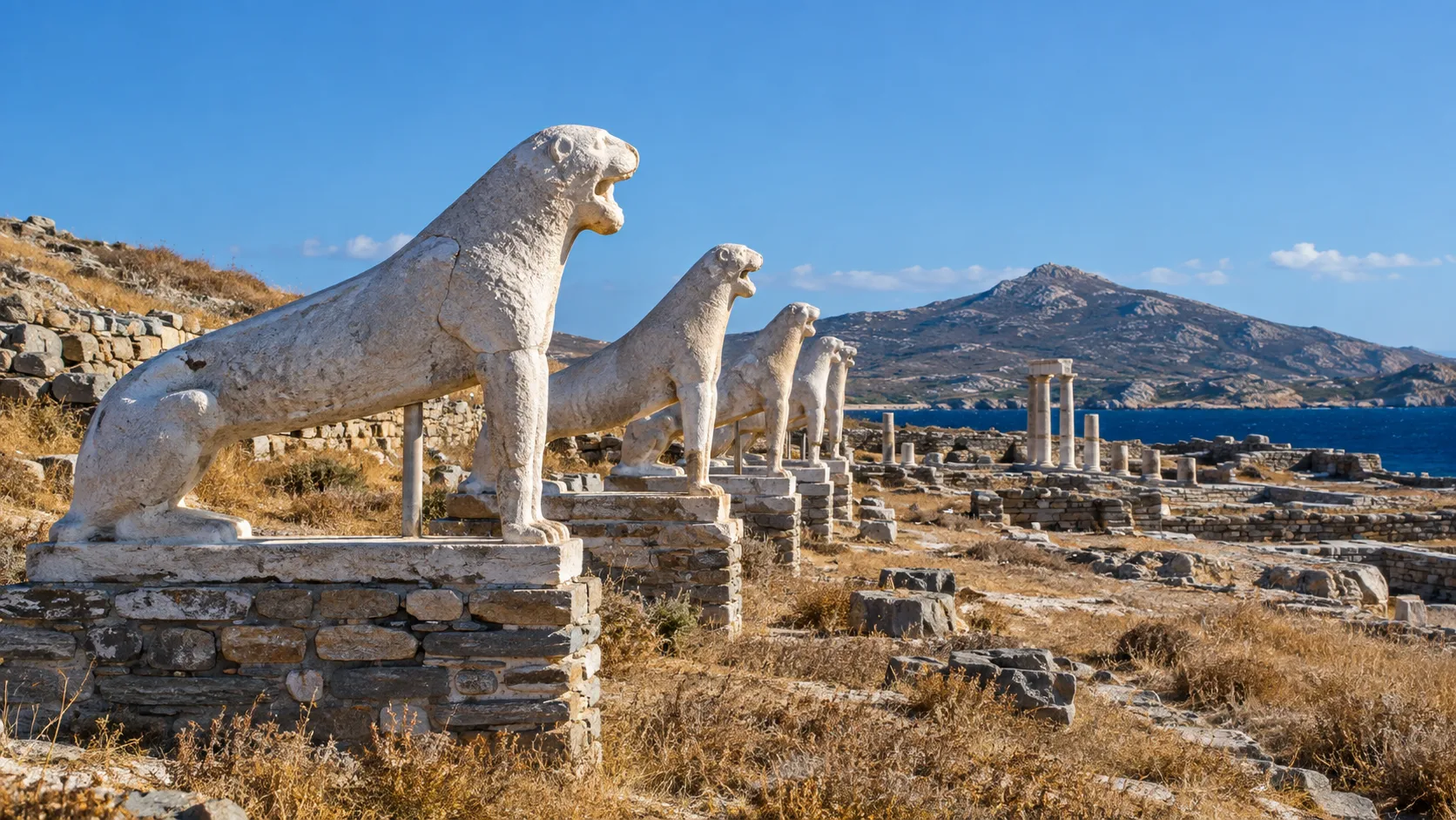 Weathered marble lions lining the Terrace of the Lions on Delos beside the blue Aegean Sea
