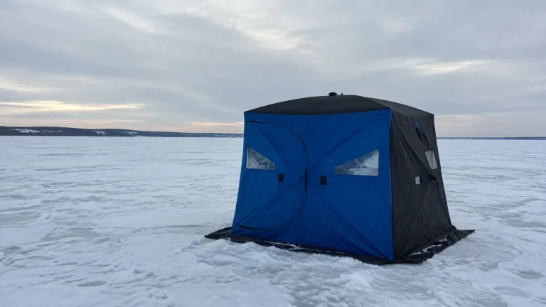 Blue ice fishing shelter stands alone on a snow-covered lake.