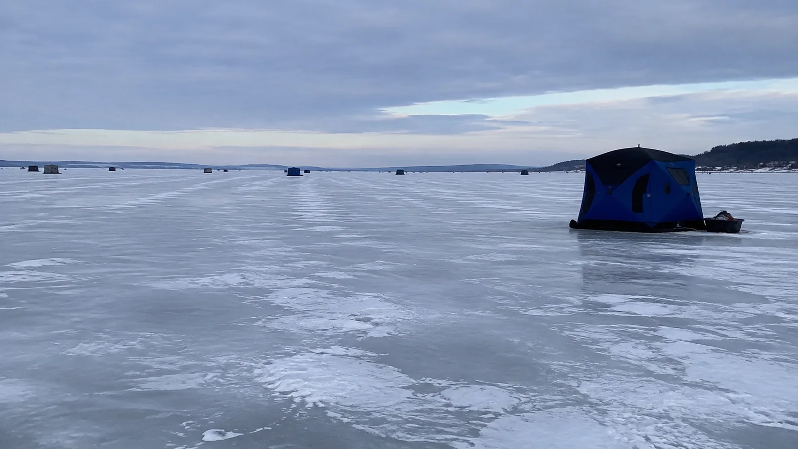 Small blue shelter on a frozen lake beneath gray clouds.