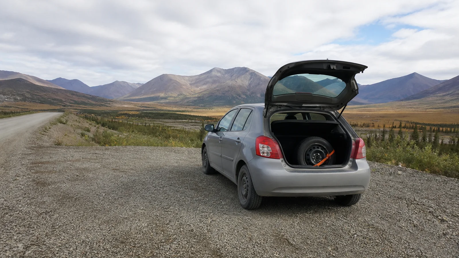 Car with open trunk parked on a remote mountain gravel road.