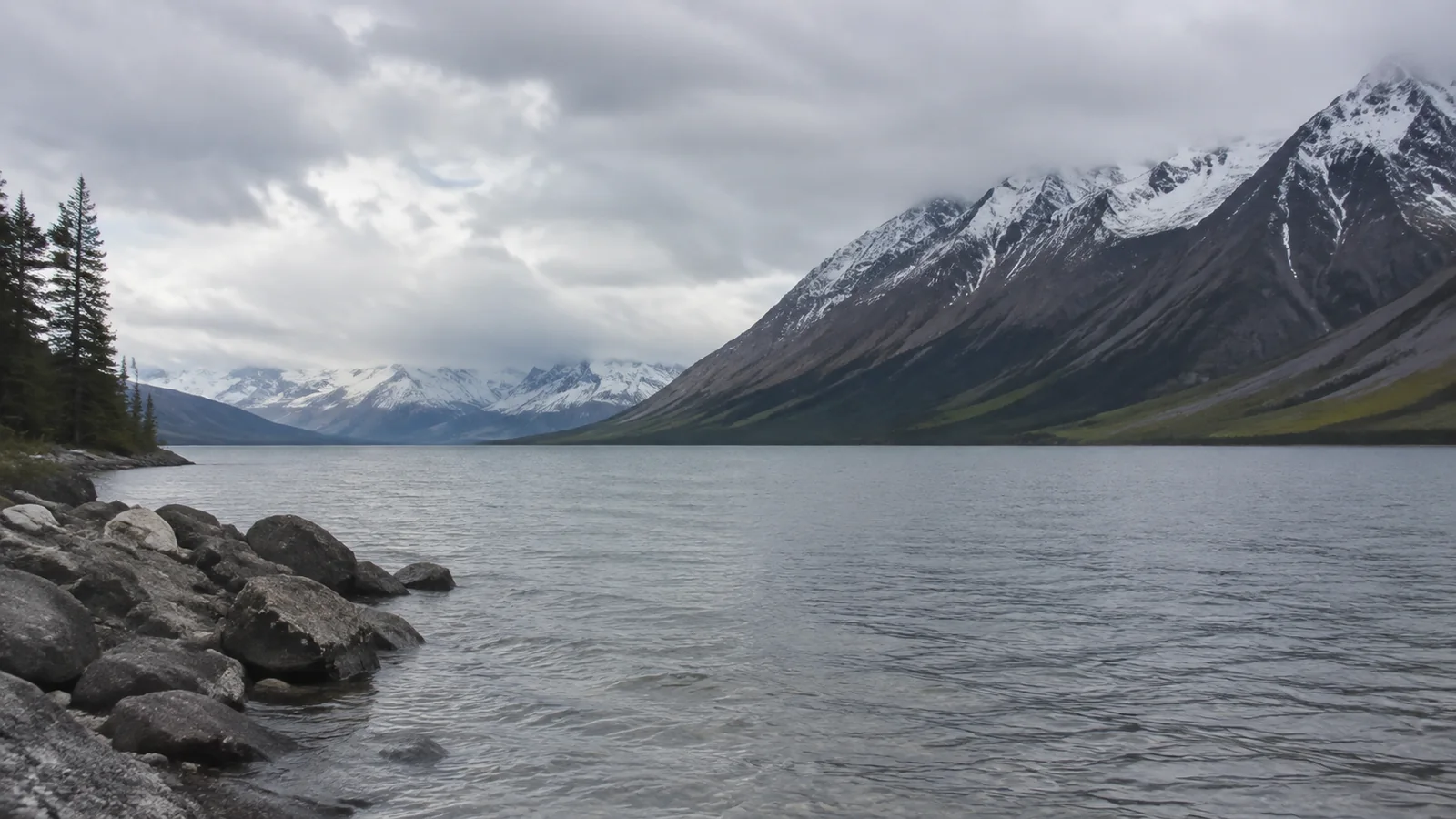 Gray lake stretches between steep snow-dusted mountain slopes.