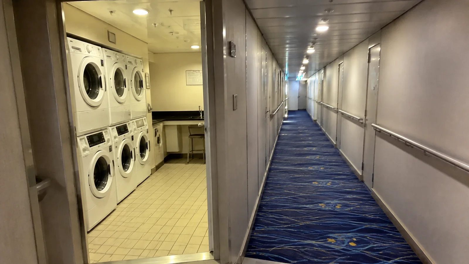 Open laundry room with stacked machines beside a cabin corridor.