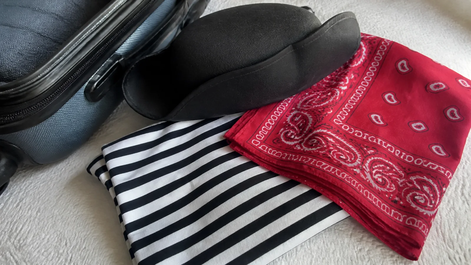 Pirate Night outfit pieces including a black hat, striped shirt, and red bandana beside luggage.