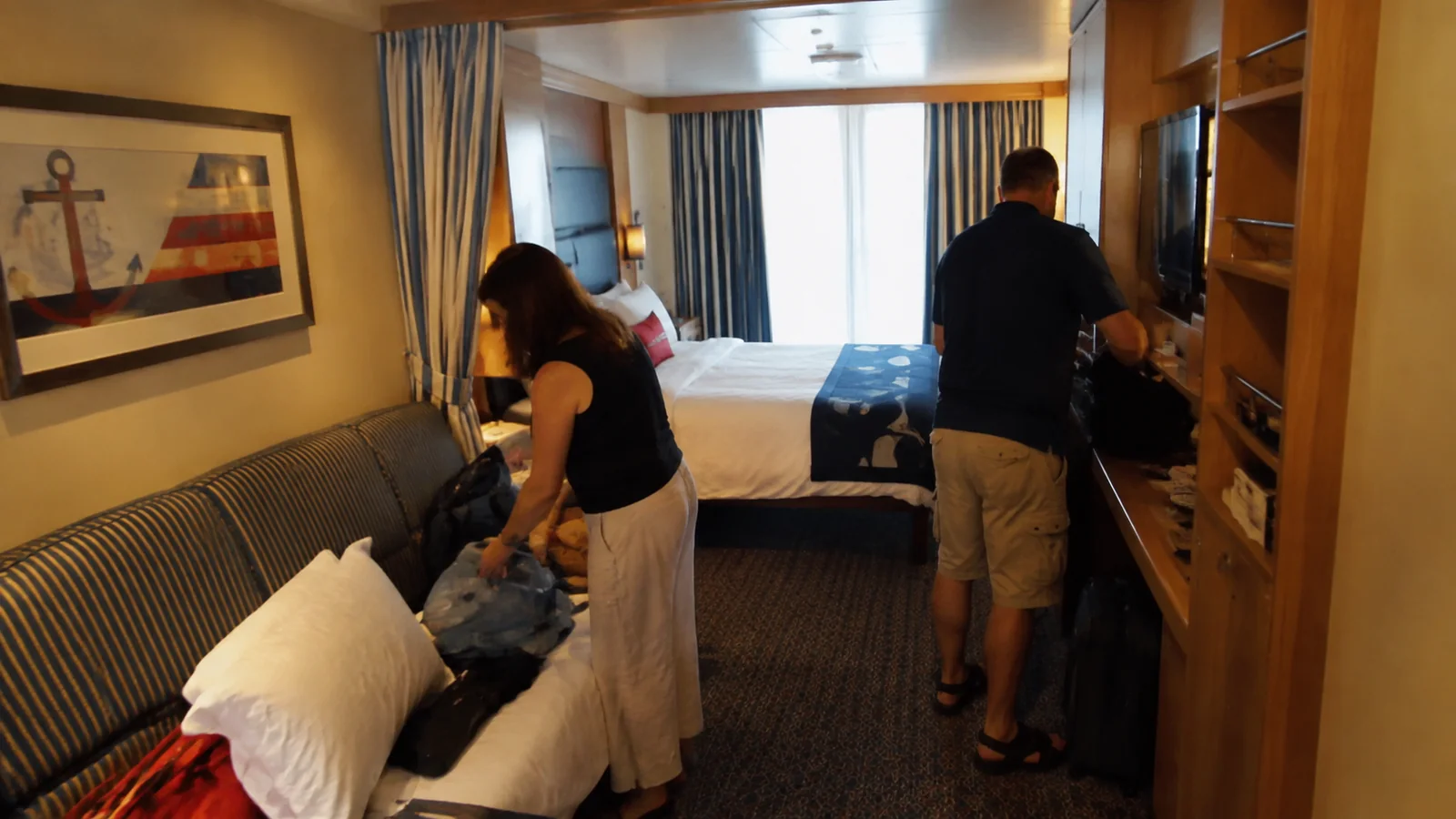 Two travelers unpack bags inside a compact cruise stateroom.