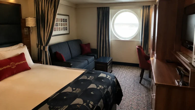 Ship cabin with a patterned bed runner, blue sofa, and round window.