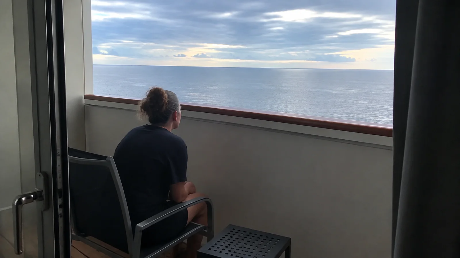 Woman seated on a sheltered balcony looking across the ocean.
