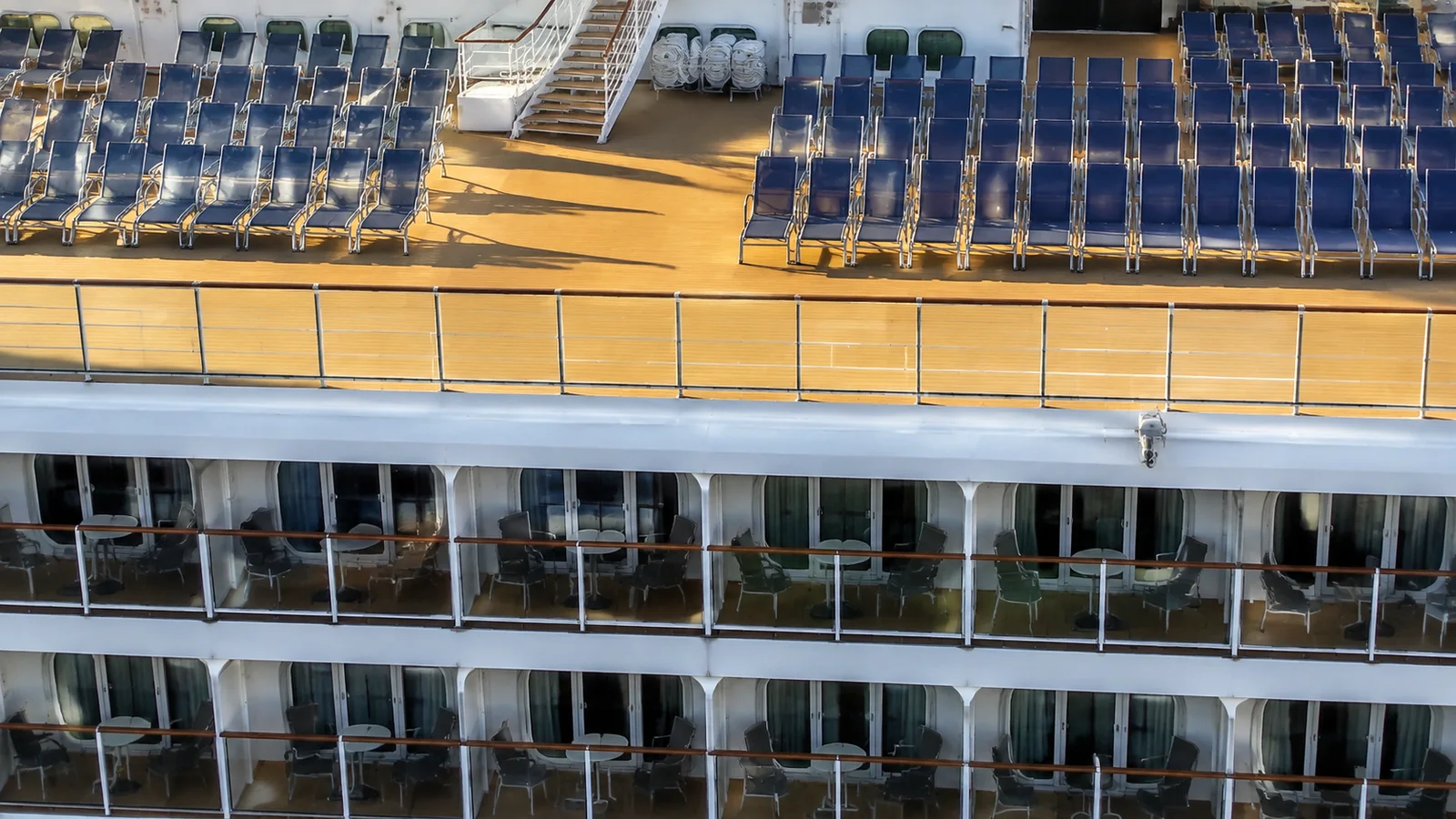Rows of balcony cabins beneath a ship deck filled with blue loungers.