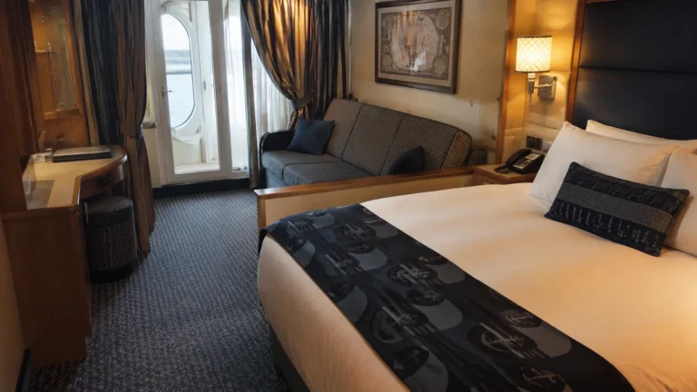 Ship cabin with a double bed, sofa, and balcony doors.