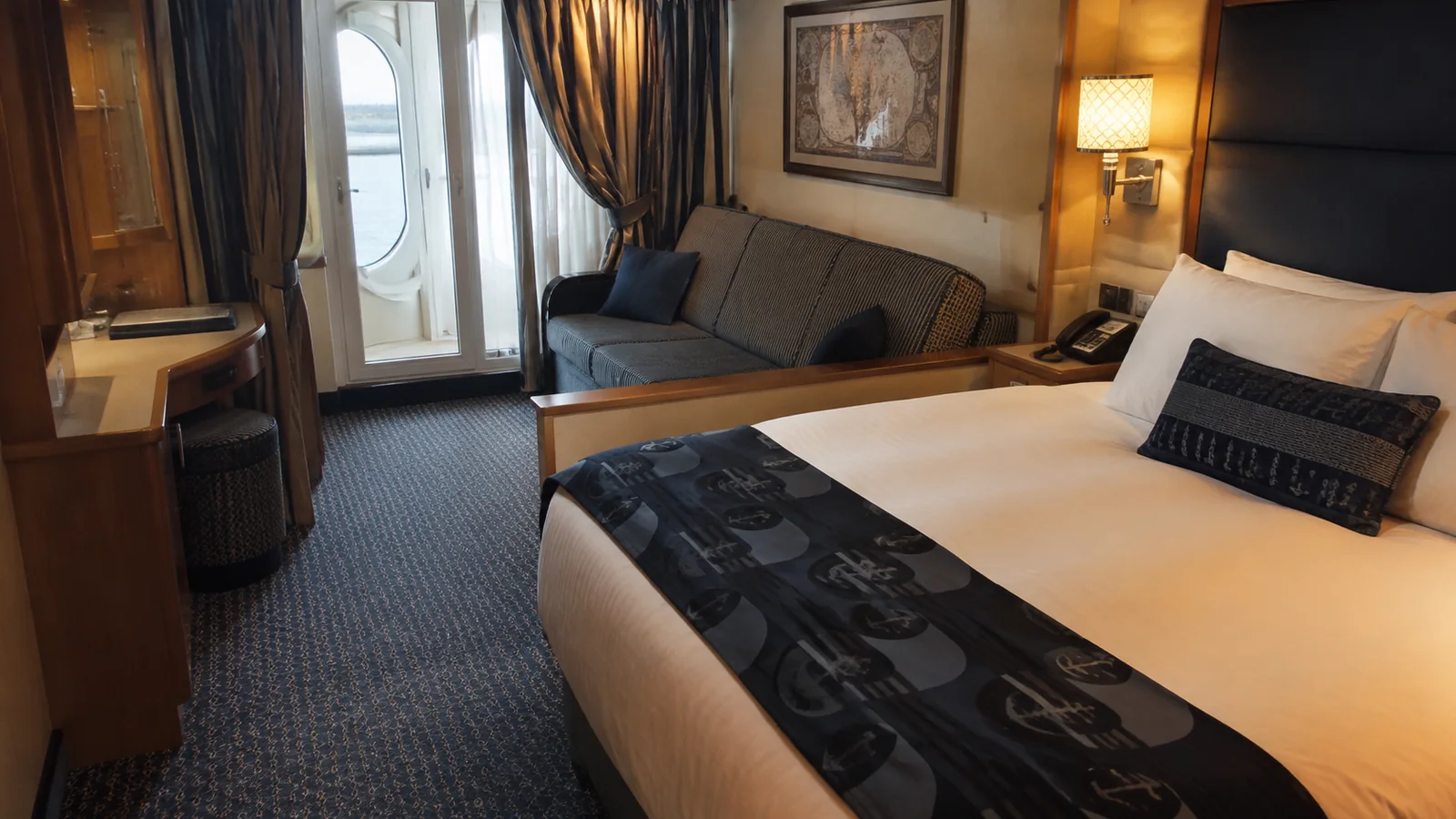 Ship cabin with a double bed, sofa, and balcony doors.