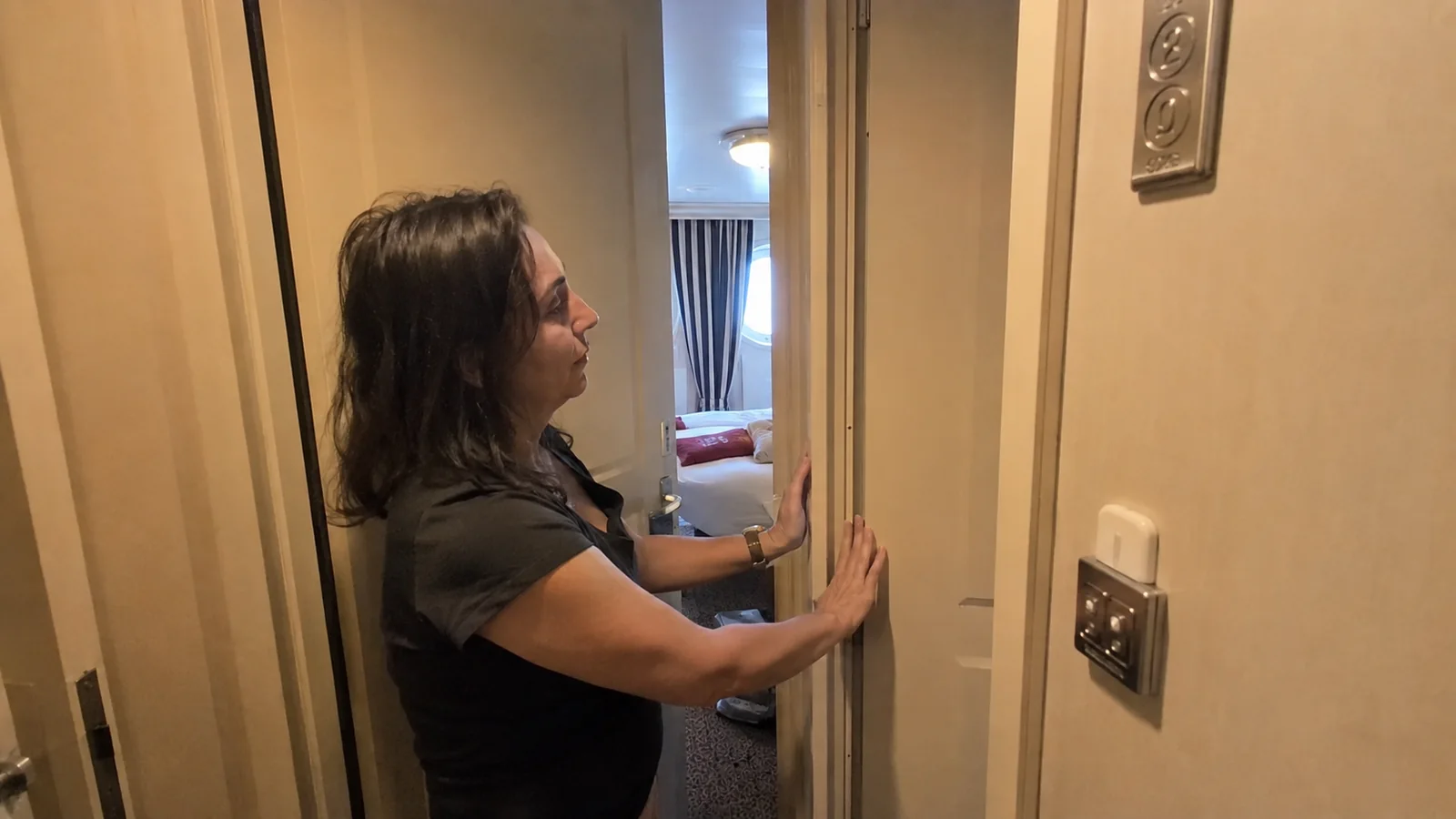 Woman examining a doorframe inside a narrow ship cabin entryway.