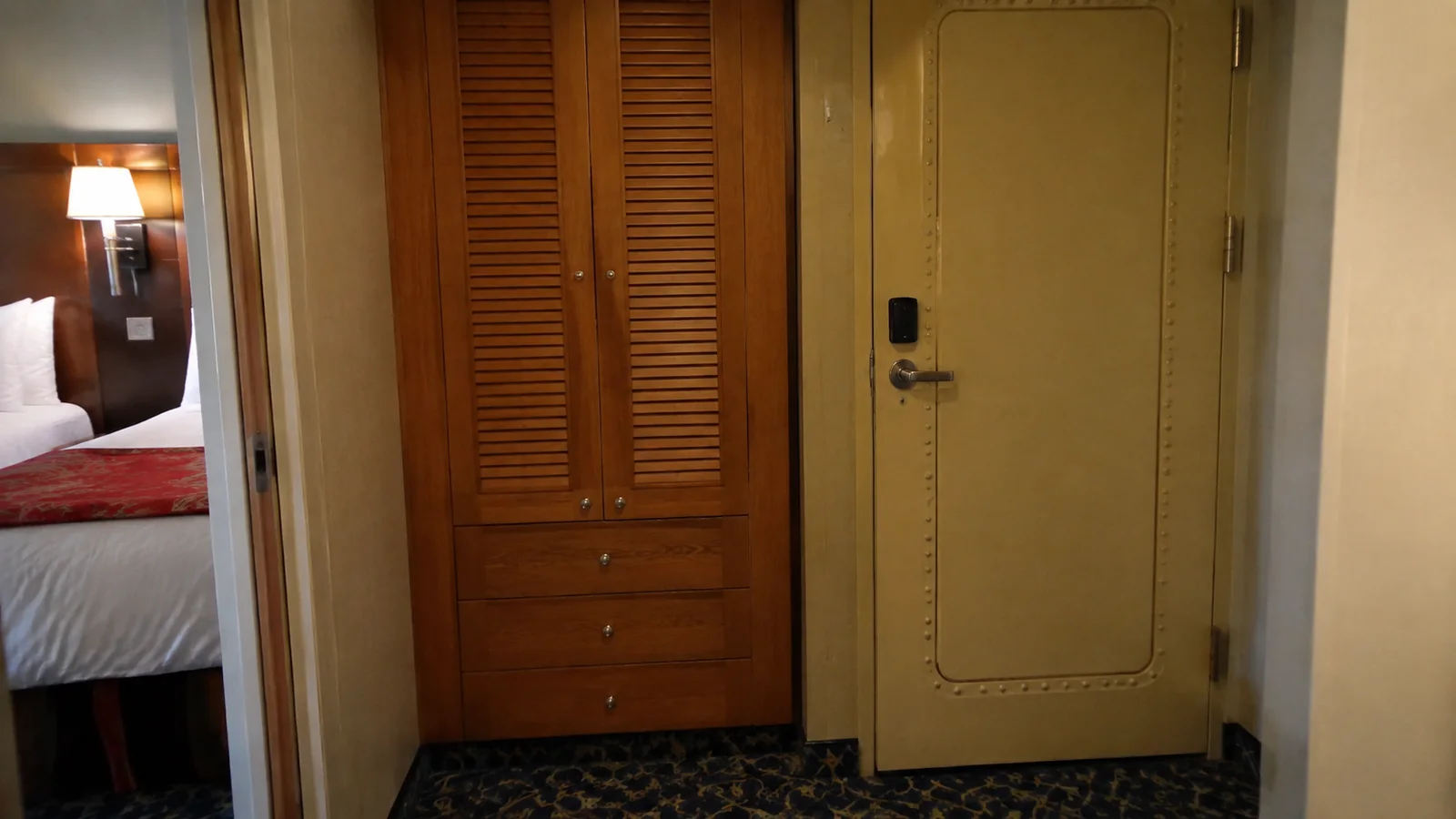Closed cabin door beside a wooden louvered wardrobe and bed.