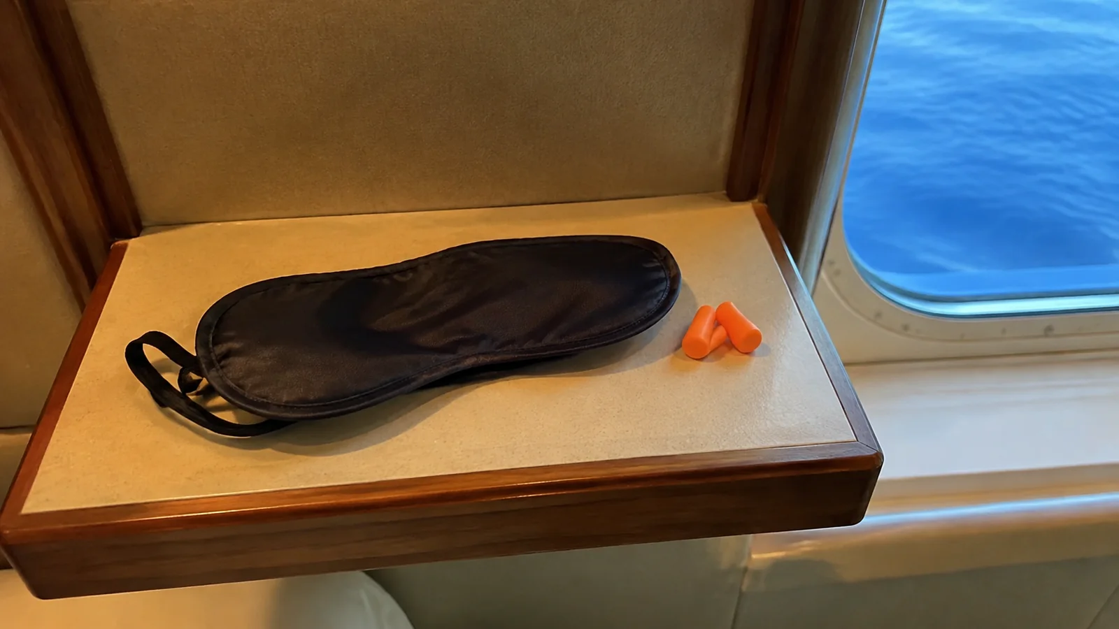 Sleep mask and orange earplugs rest beside an ocean window.