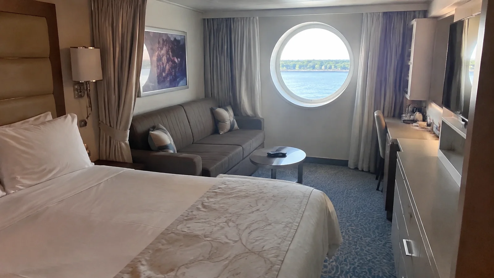 Stateroom has a double bed, sofa and round ocean window.