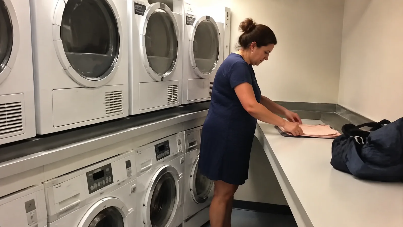 Woman folds clothing on a counter beside stacked laundry machines.