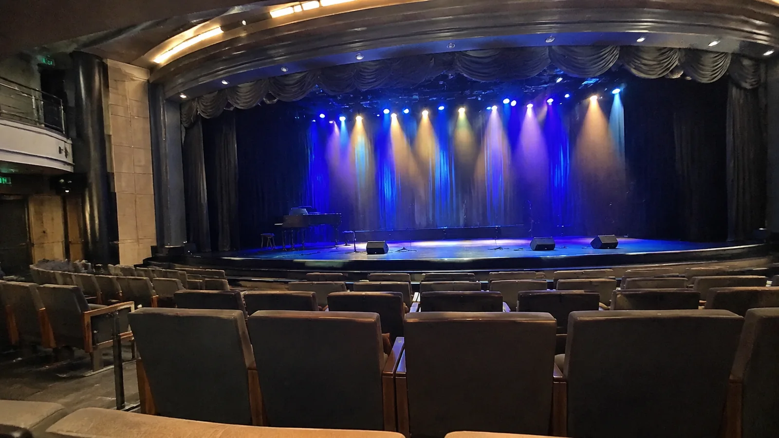 Empty theater seats face a stage illuminated with blue spotlights.