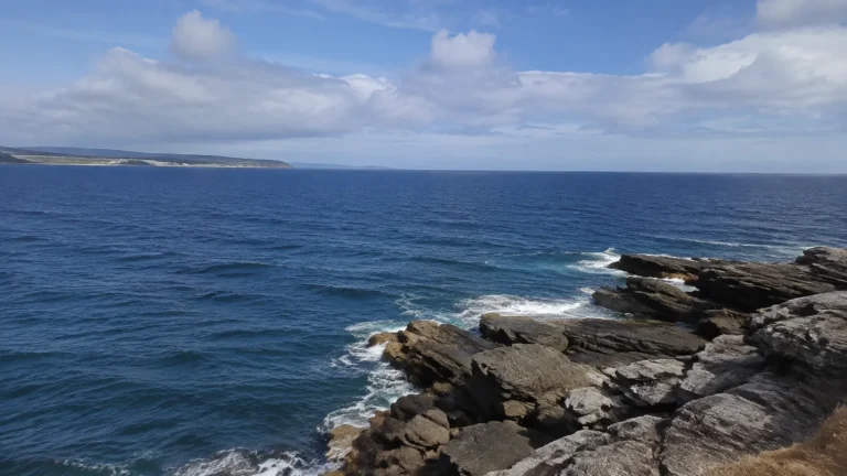 Blue ocean extending beyond a rugged layered rock shoreline.