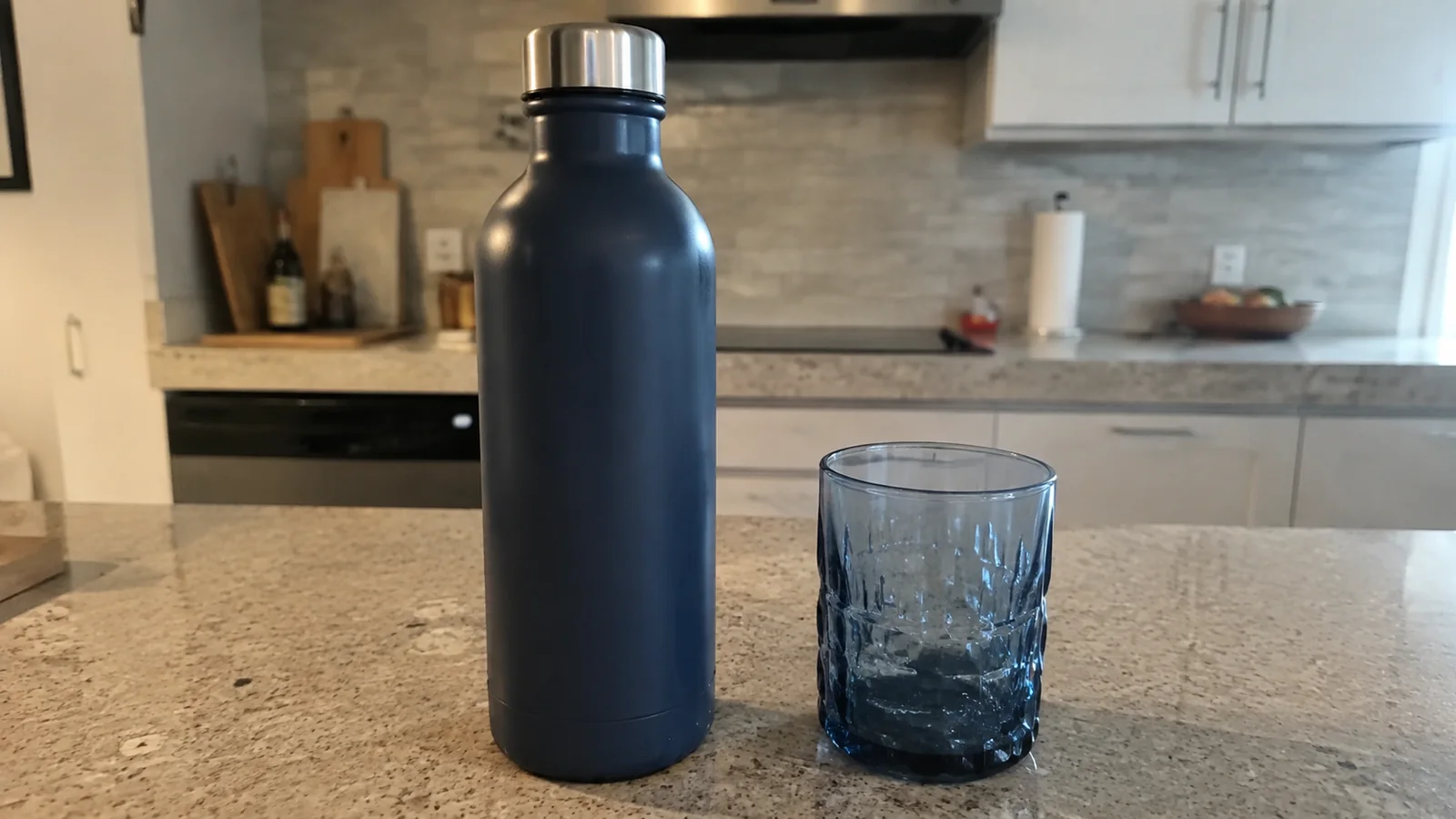 Blue metal water bottle and drinking glass on a kitchen counter.