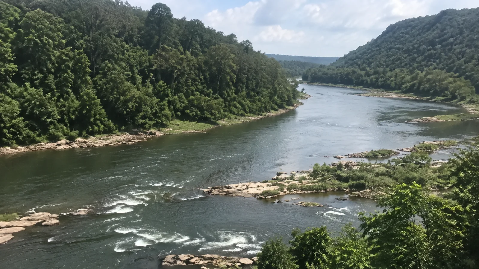River flowing between forested hills and exposed rocky banks.