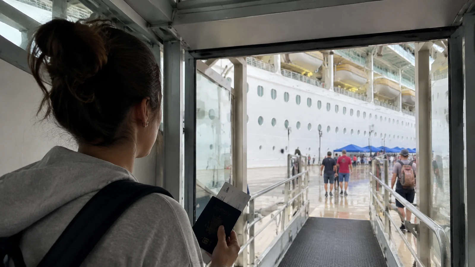 Passenger holding travel documents while walking along a gangway toward a cruise ship