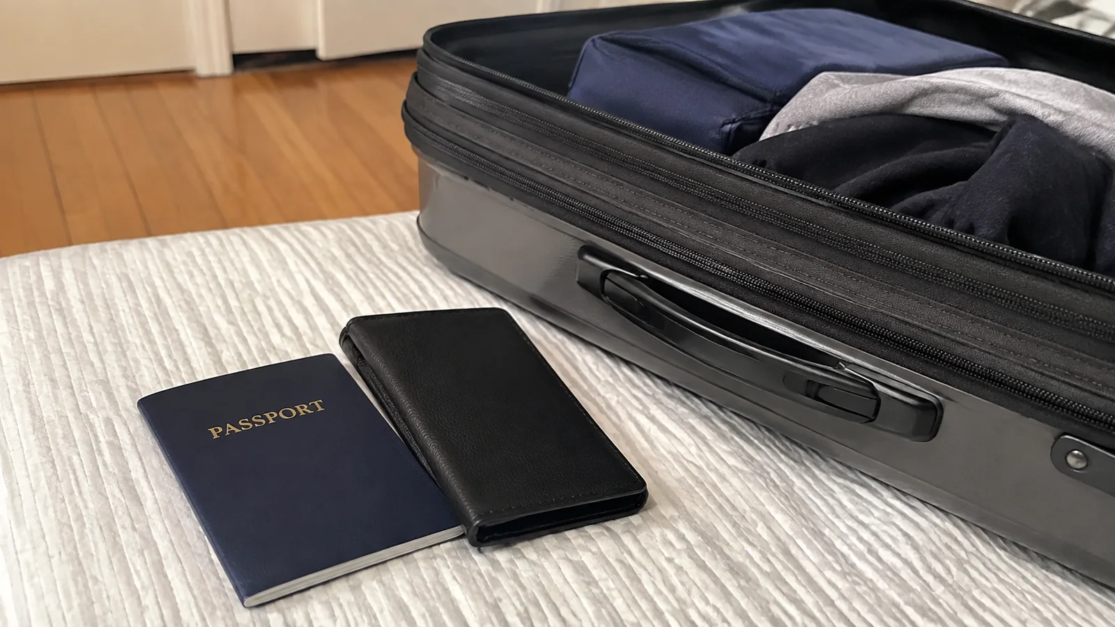 Passport and black document wallet beside an open suitcase.