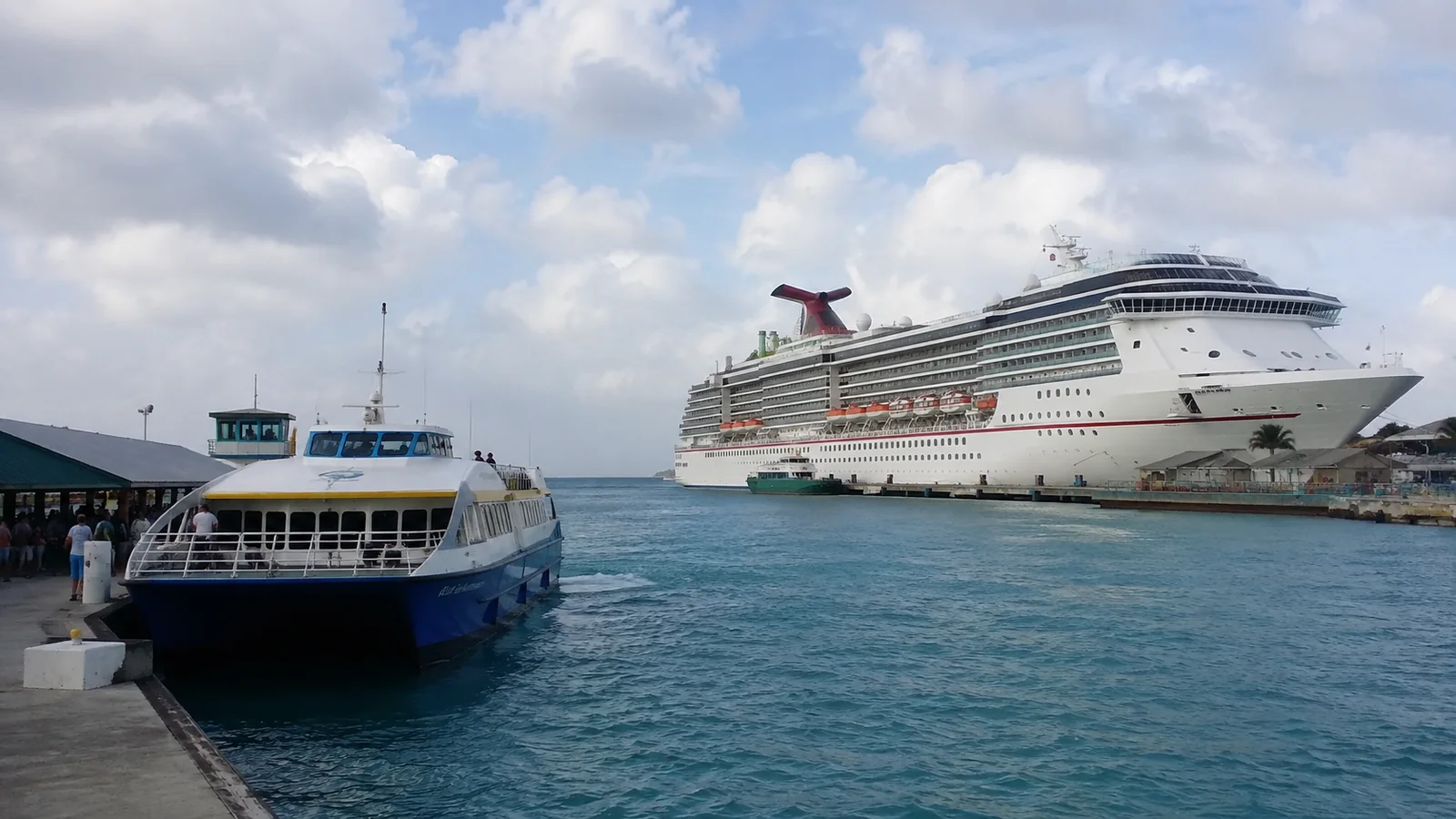 Passenger ferry and large cruise ship in a turquoise harbor.
