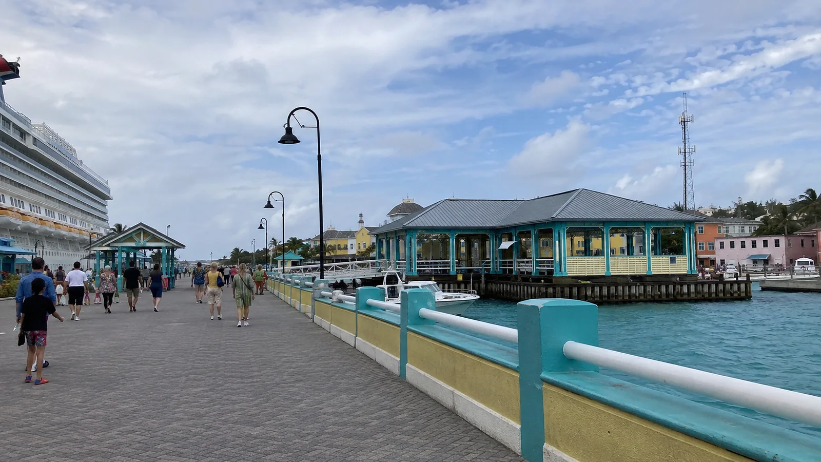 Passengers walking along a turquoise-railed cruise pier.