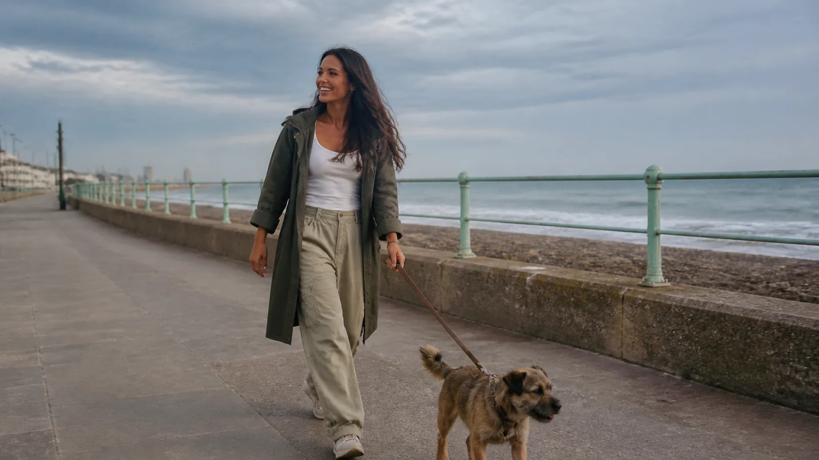 Woman walks a small dog along a seafront promenade.