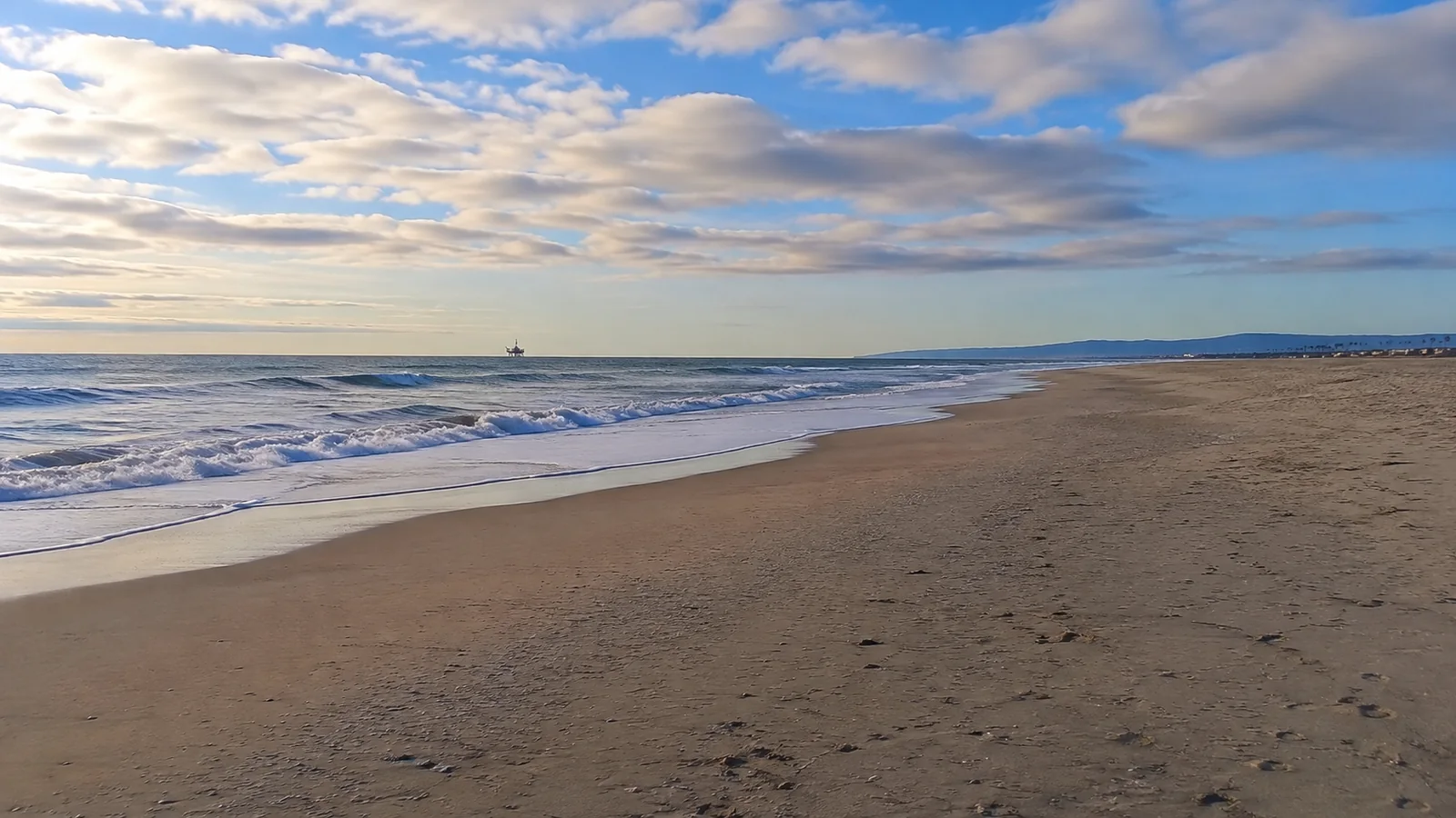 Broad sandy beach and gentle surf beneath a pastel evening sky.