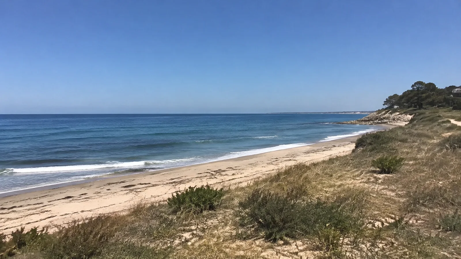 Coastal dunes border an empty beach and deep blue sea.