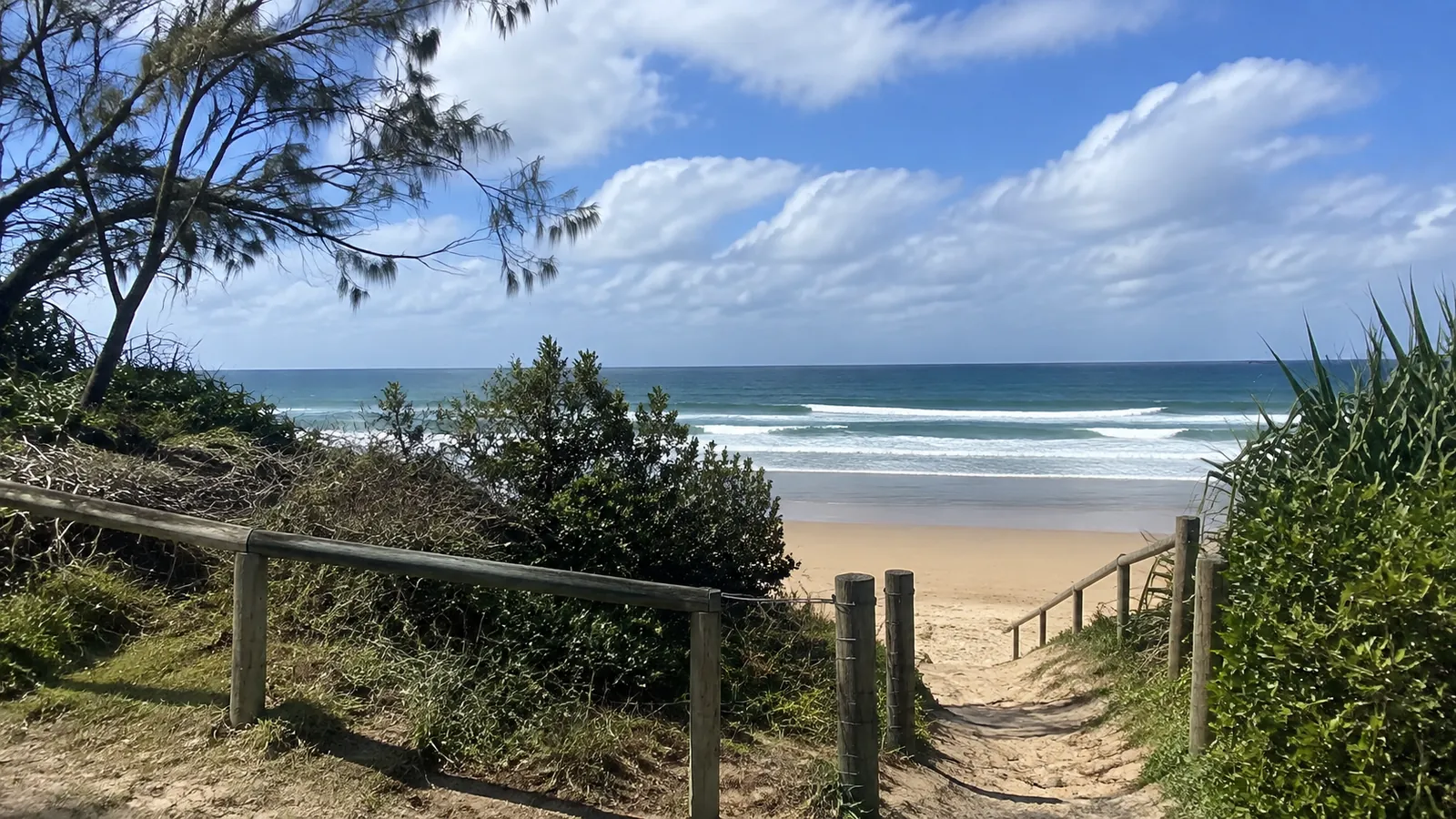 Sandy beach access path descends between railings toward the surf.