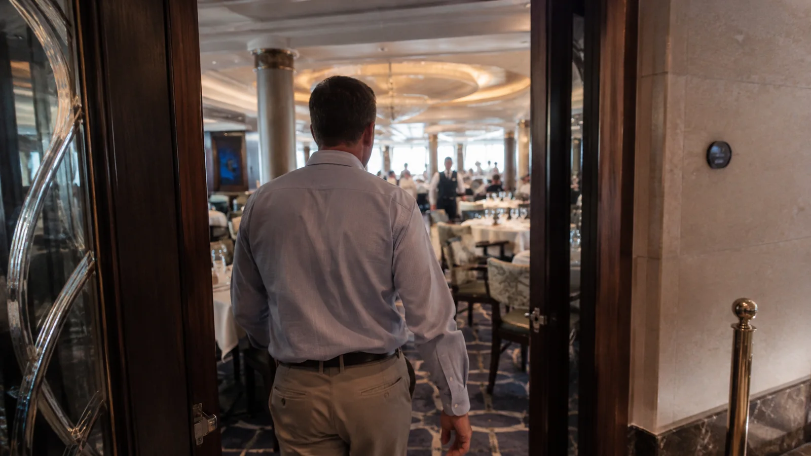 Passenger in a collared shirt and trousers entering a ship dining room.
