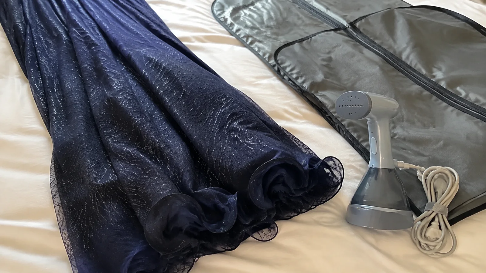 Navy dress and handheld garment steamer beside an open suitcase