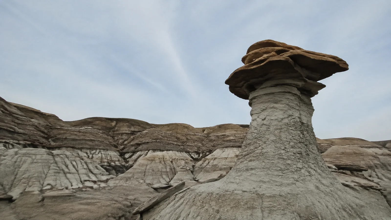 Mushroom-shaped hoodoo with a broad dark cap above pale layered rock.