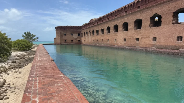 Long red brick fort wall beside clear turquoise water.