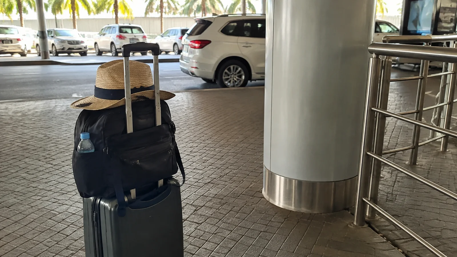 Suitcase with a backpack and sunhat beside a terminal taxi area.
